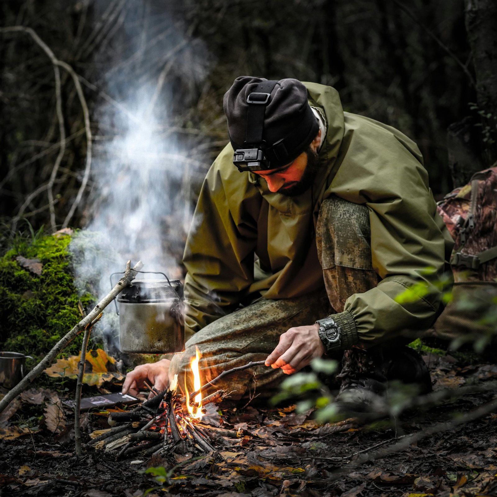A man kneels in a forest while skillfully starting a campfire, showcasing survival skills.